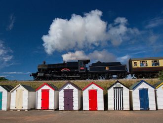 http://Dartmouth%20Steam%20Railway,%20train%20travelling%20above%20beach%20huts%20in%20Paignton,%20Devon.