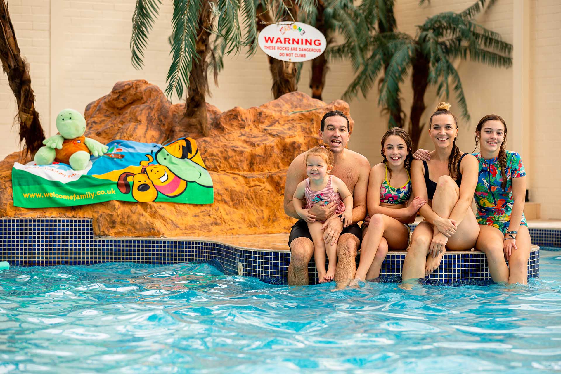 Family sitting by pool edge at Welcome